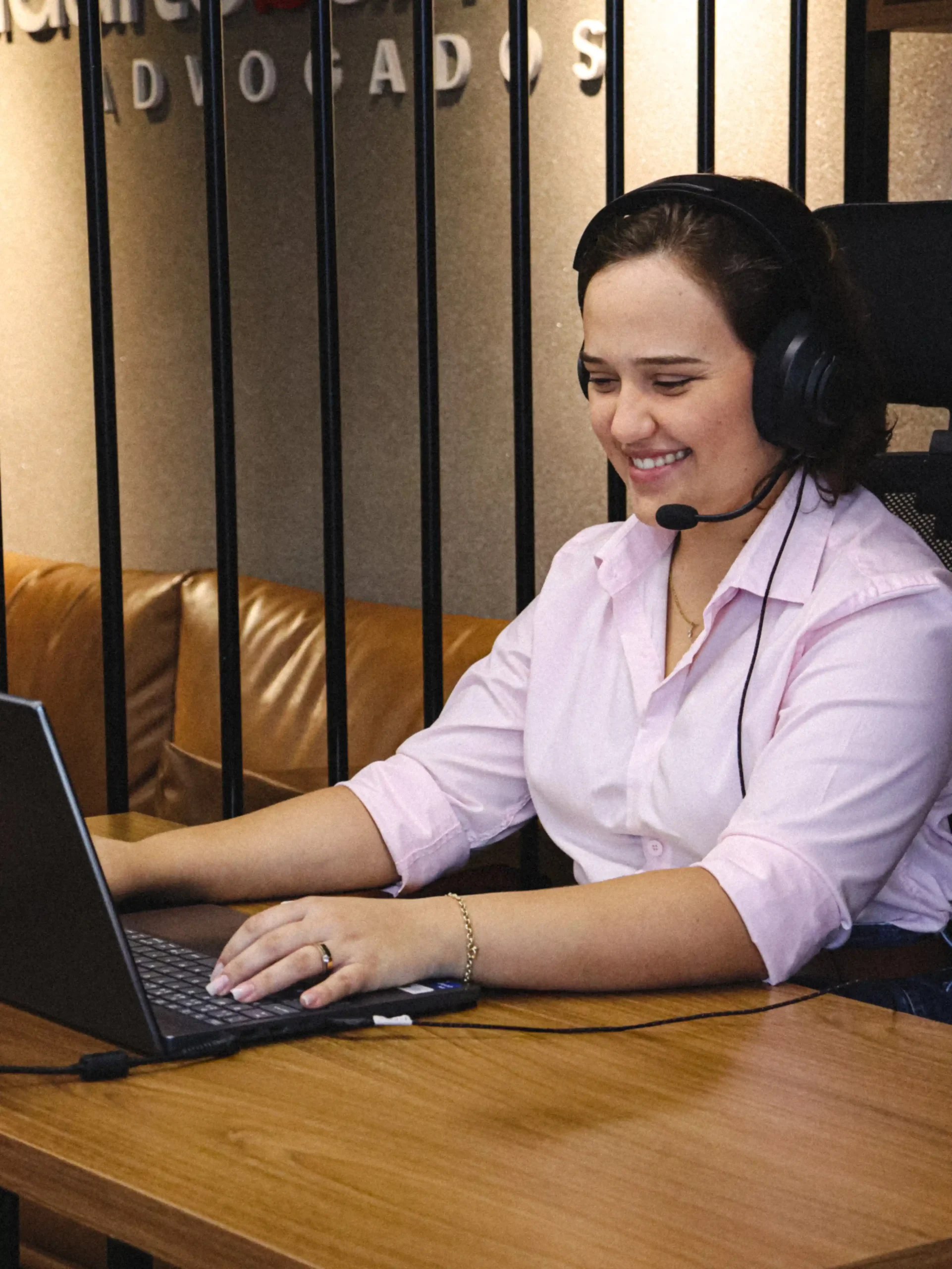 Integrante do escritório de camisa rosa e headset sorrindo durante atendimento no notebook