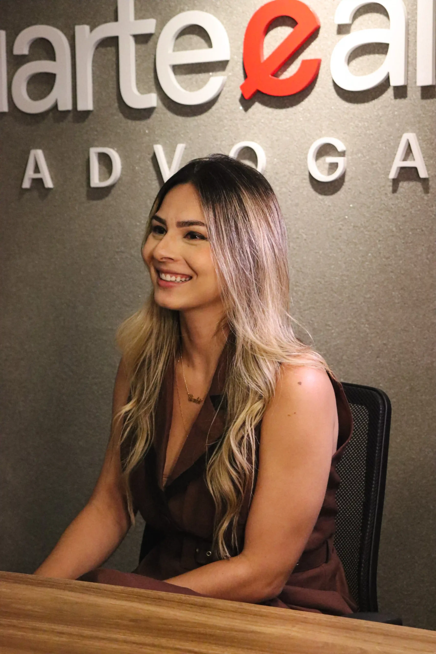 Integrante do escritório sorrindo sentada à mesa diante do letreiro da marca