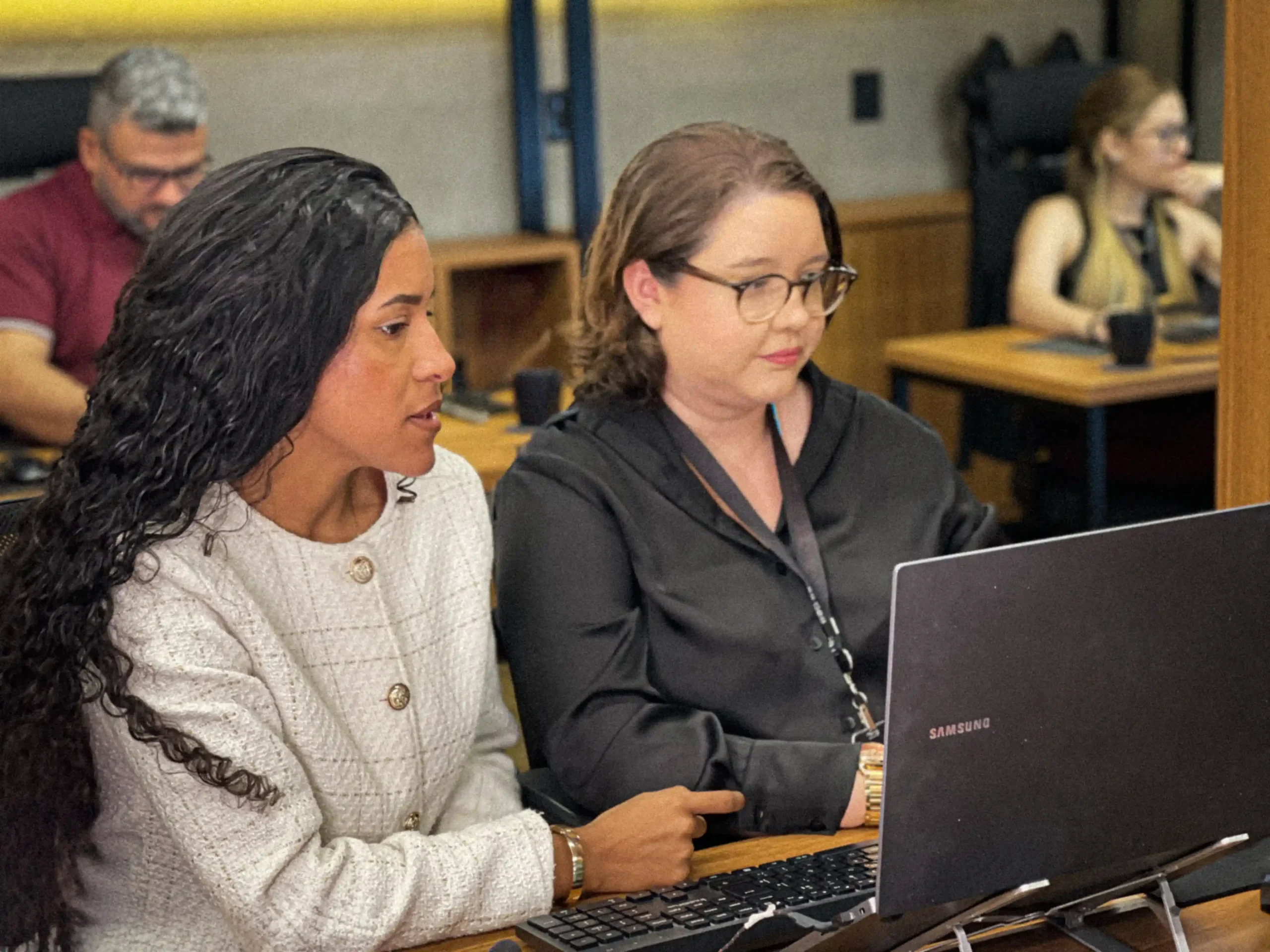 Duas integrantes do escritório discutindo um processo diante do notebook