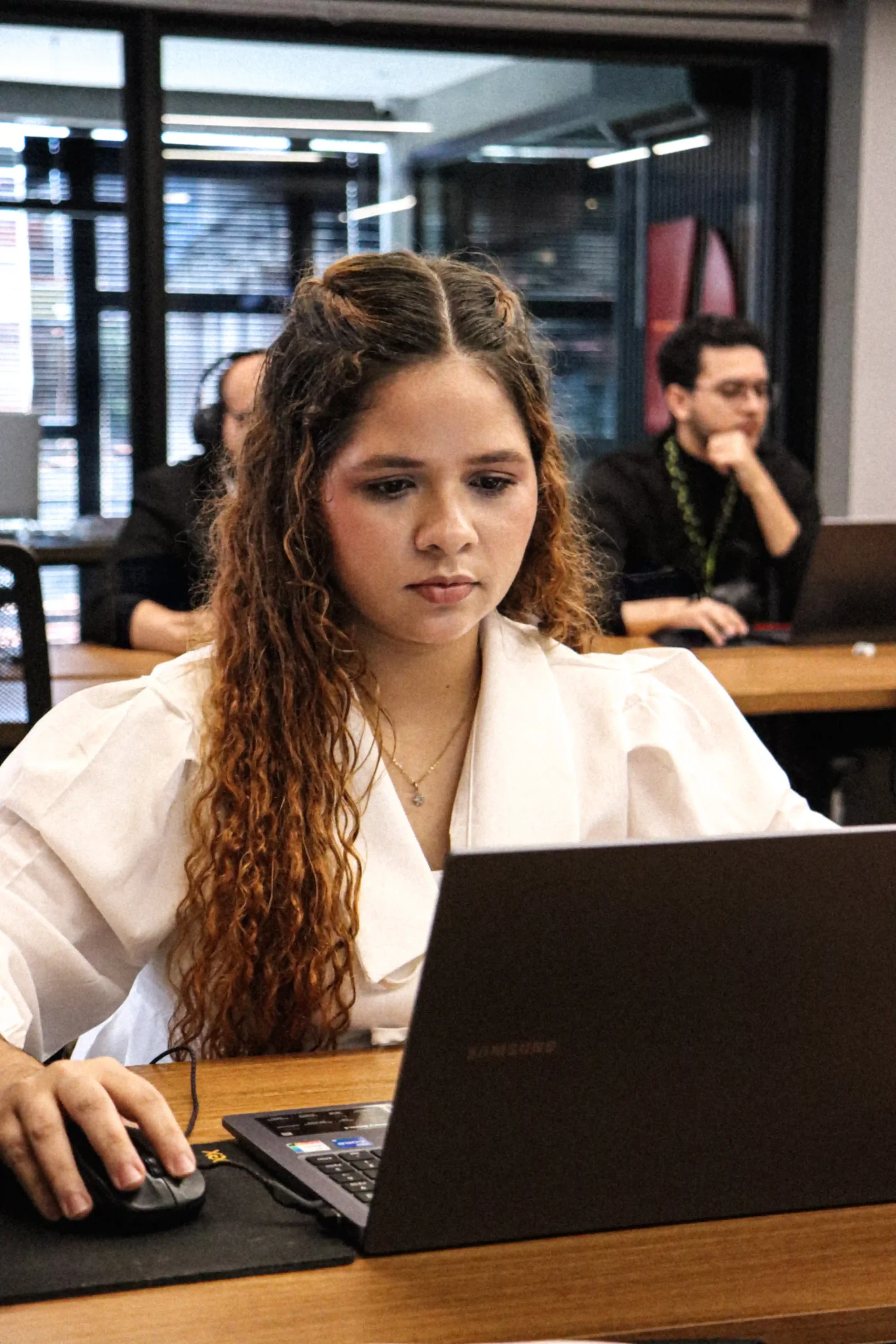 Integrante do escritório de blusa branca concentrada no notebook em sala compartilhada