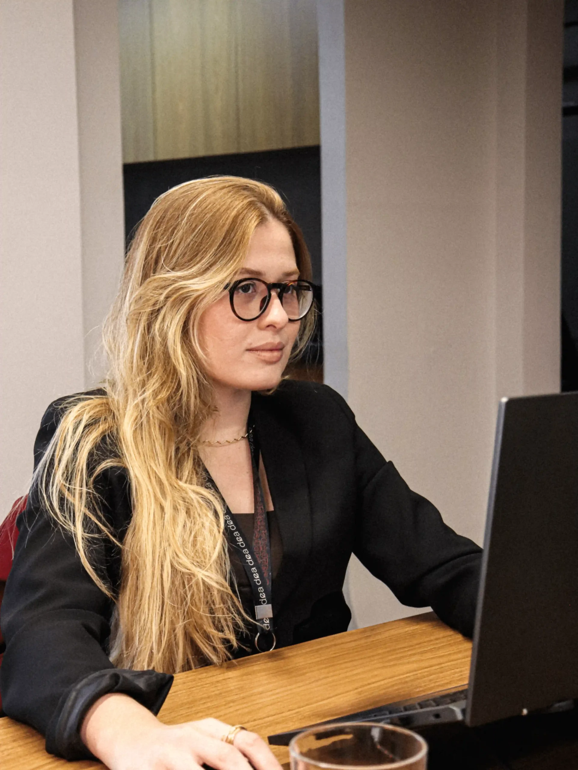 Integrante do escritório de blazer preto, óculos e crachá concentrada no notebook