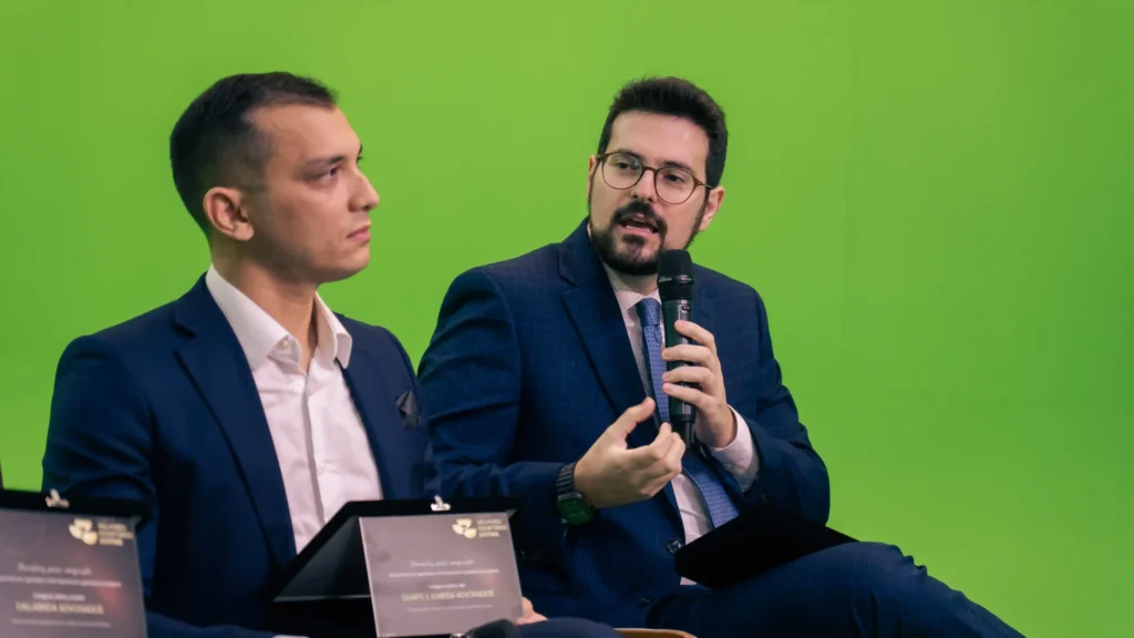 Dois participantes do Law Summit debatendo, um deles ao microfone, em estúdio de chroma key