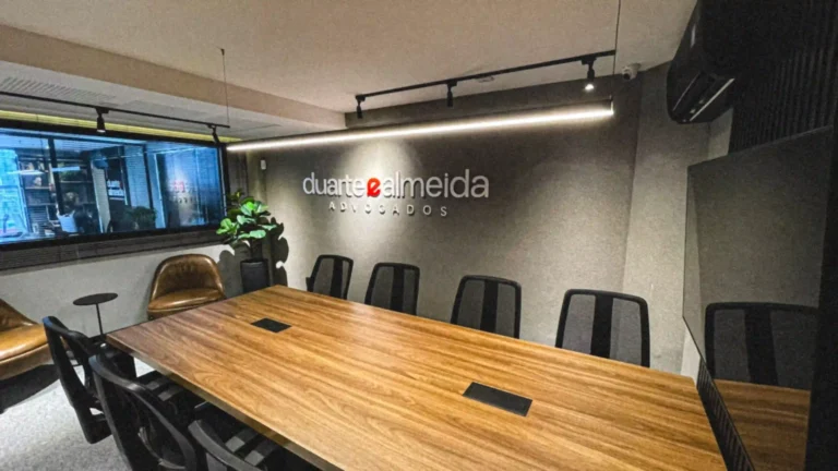 Sala de reunião do Duarte e Almeida Advogados com mesa longa, marca na parede e painéis de vídeo